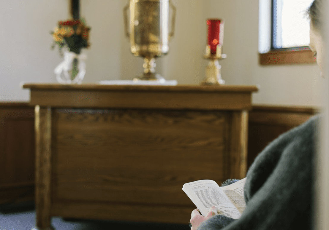 A woman praying at a prayer space in her home. She is reading a Bible. 